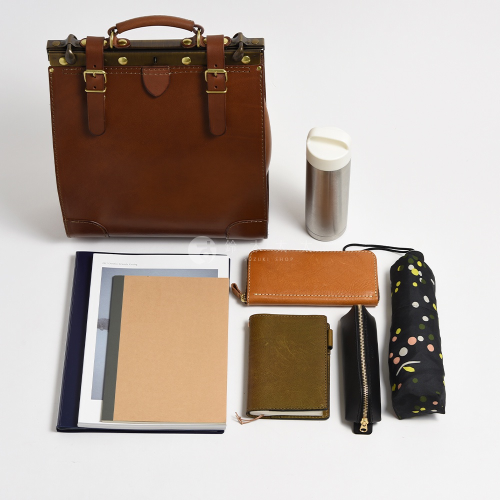 職人手作皮革復古口金後背包，搭配一個銀色保溫瓶、一個棕色長夾、一個綠色筆記本、一個黑色筆袋，以及一個印有彩色圓點圖案的摺疊傘。