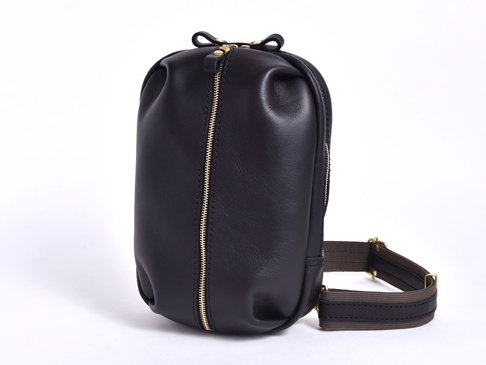 職人手作黑色皮革立體運動斜背包，設有金色拉鍊和織帶背帶，風格簡約實用。