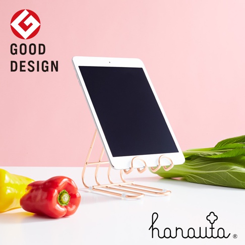 玫瑰金色不鏽鋼萬用支架，以簡約線條支撐著一台平板電腦，支架上有兩個捲曲的支撐點，整體風格時尚。