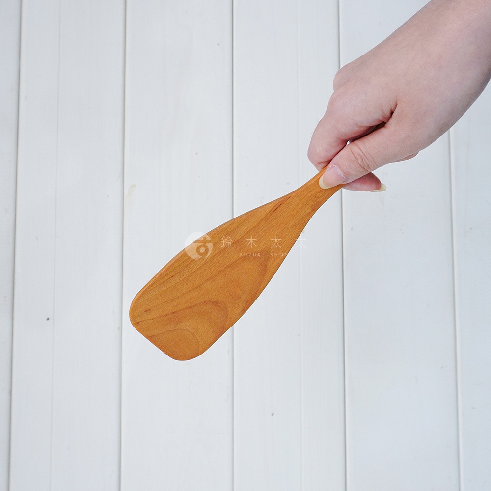 一隻手正拿著一個木質鍋鏟，鍋鏟呈淺木色，帶有細緻的木紋，末端為橢圓形，適合攪拌使用。