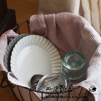 鐵籃裡裝著粉色鬆餅紋布巾，其中有疊放的白色和灰色盤子，以及兩個玻璃杯。