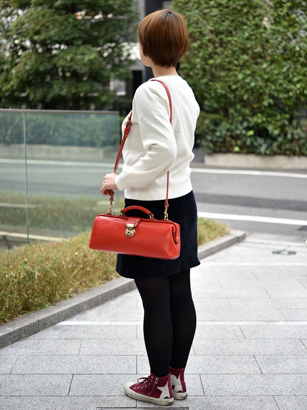 亮橘色皮革橫長形單肩包，具備金色鎖扣和手提把，可斜背或手提。