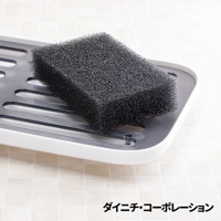 一個深灰色海綿塊放置於白色邊框的灰色濾水架上，濾水架具有條狀紋路和圓形孔洞。