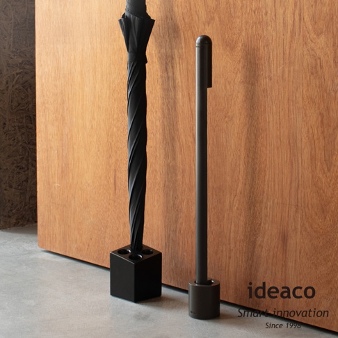 ideaco 品牌立扇，黑色傘架上放著一把黑色傘，旁邊有一個長柄鞋拔，品牌名稱 ideaco 和口號 Smart innovation Since 1998 印在右下方。