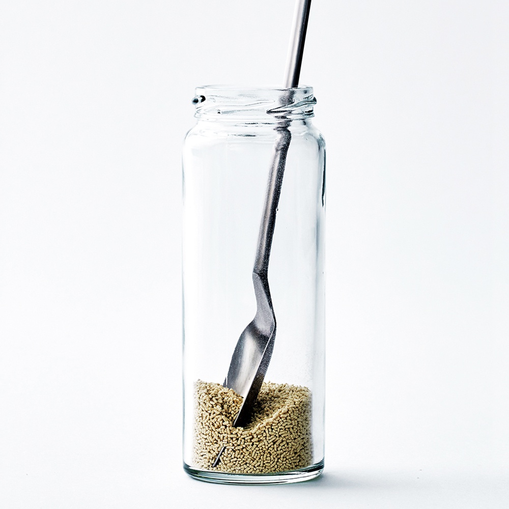 日製小長勺，銀色金屬材質，勺頭呈扁平狀，插入裝有淺黃色顆粒的透明玻璃瓶中。