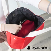 一位女子手提紅色帆布托特包，包內有一個小化妝包，包帶為白色。