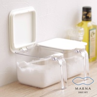 兩個透明塑膠調味料盒，每個約600ml容量，裝有白色粉末。盒蓋為白色，其中一個盒蓋打開。塑膠提把透明，方便拿取。背景為白色牆壁與木質桌面，右側有黃色瓶裝液體。