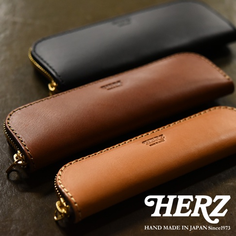 三款不同顏色的職人手作皮革筆袋，分別為黑色、棕色和焦糖色，以拉鍊封口，上面壓印有品牌標誌。