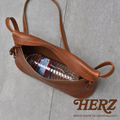 一個棕色皮革製成的斜背包，裡面裝著一瓶水。