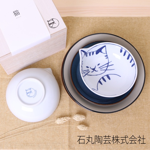 木盒包裝的貓咪飯碗四入組。其中兩個飯碗為白色陶瓷，其中一個碗內繪有藍色線條的貓咪圖案，另一個碗底部有藍色貓咪標誌。另有兩個深藍色和灰色的陶瓷碗疊放。