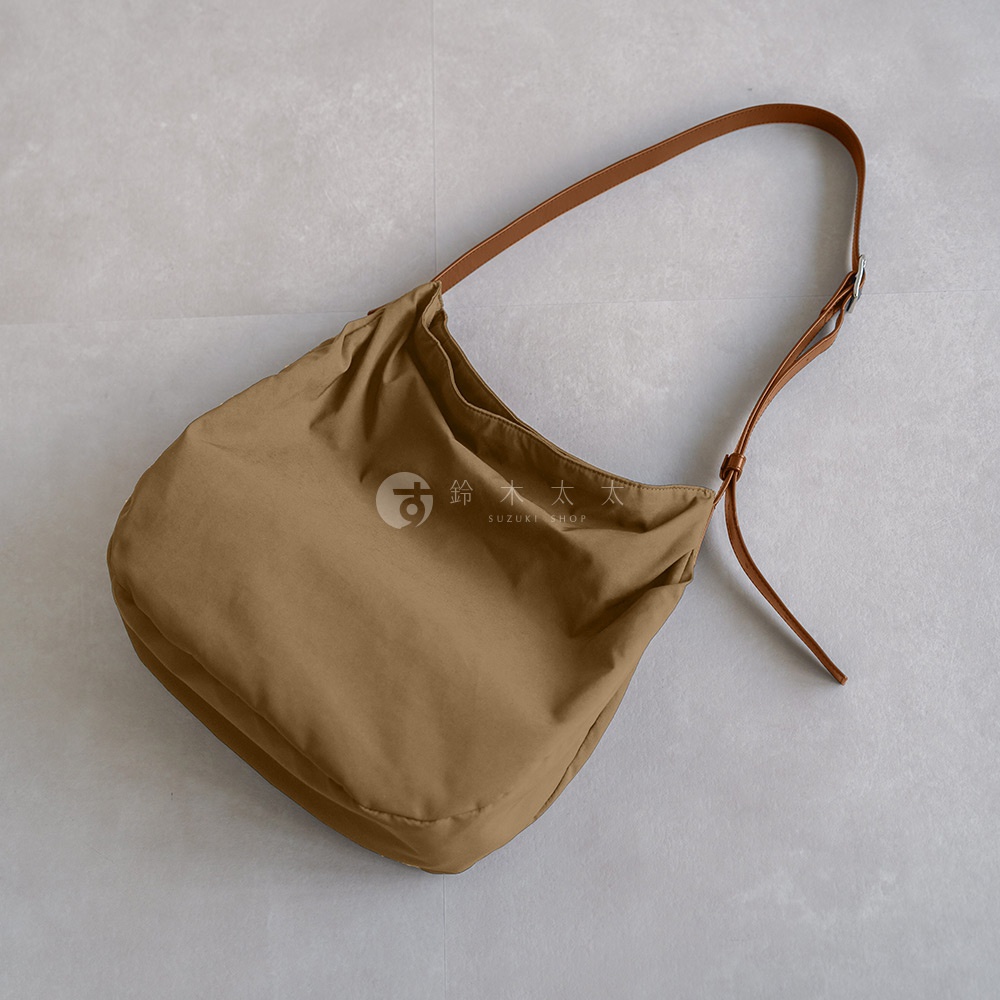 Attelier nuu 棕色尼龍托特包，配有棕色皮革肩帶，包上印有品牌標誌和文字。