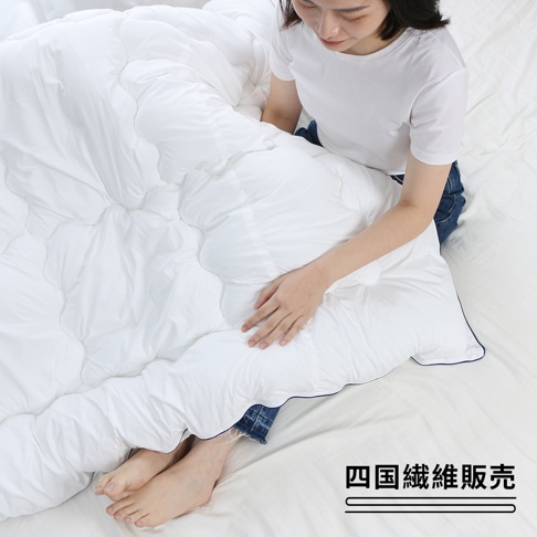 雙人SOFAIR無重力空氣被，白色，蓬鬆中棉填充，被面有波浪形縫線，深藍色滾邊，一位女士坐在被子上。