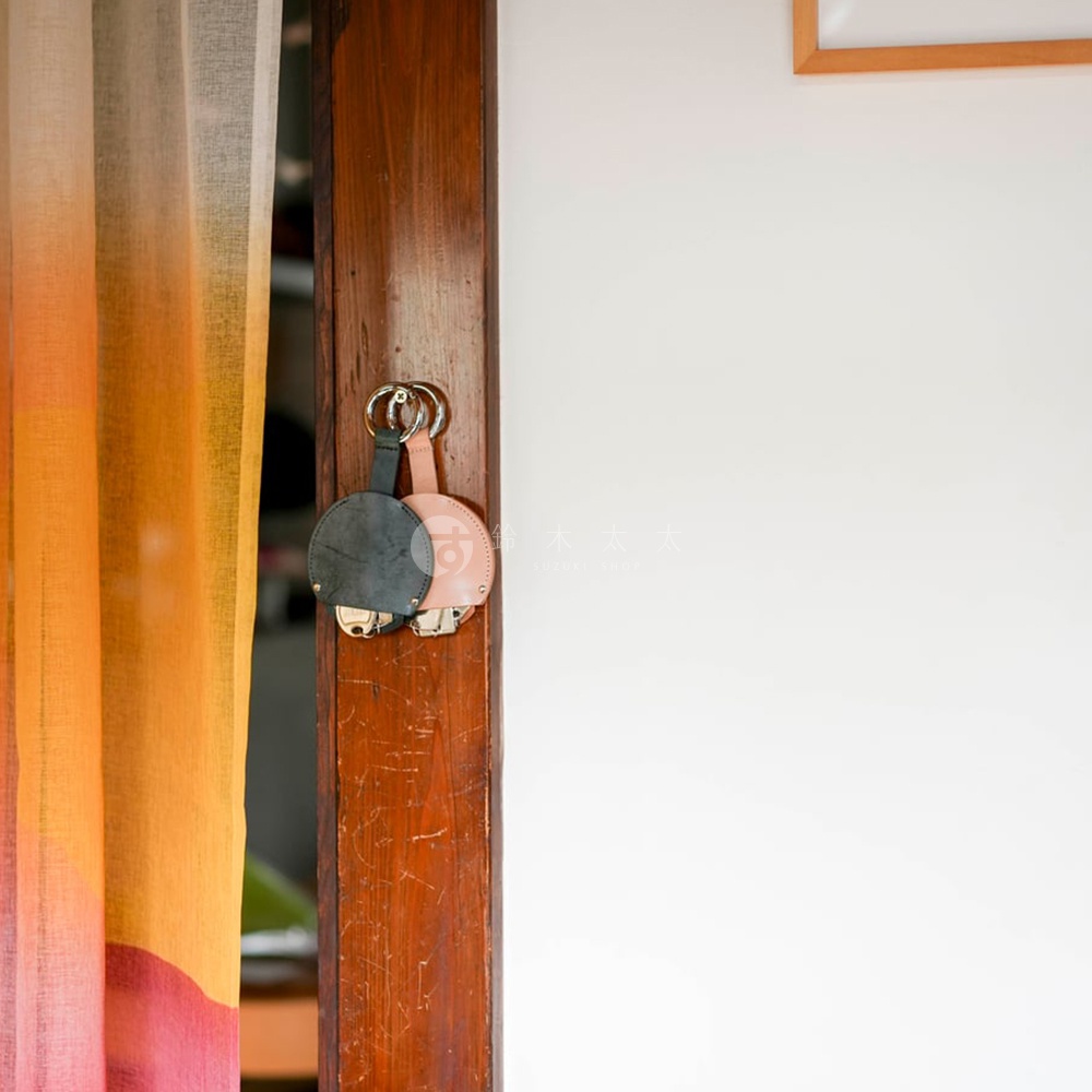 FABRIK 皮革圓型收納鑰匙圈，懸掛於木門框，左側為漸層橘粉色窗簾