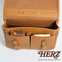 職人手作皮革商務休閒兩用單肩包，採用淺棕色牛皮製作，內部有拉鍊小包、筆槽及文件隔層，外觀有兩組金屬釦帶，質感細緻，設計簡約實用。