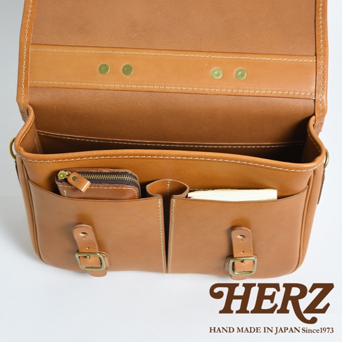 職人手作皮革商務休閒兩用單肩包，採用淺棕色牛皮製作，內部有拉鍊小包、筆槽及文件隔層，外觀有兩組金屬釦帶，質感細緻，設計簡約實用。