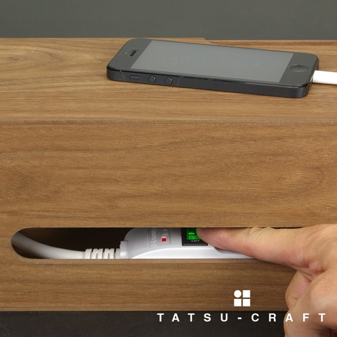 木色集線收納盒，展示一個手機放在盒頂，手指伸入側邊槽內操作延長線開關。