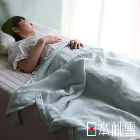 一位女性仰躺在床上，蓋著一條淡藍色的二層紗單人毯。毯子材質輕柔，紋理清晰可見，邊緣有細緻的縫線。
