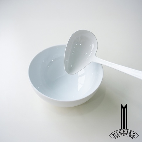 簡潔的白色湯碗旁，一個同色系的湯勺，勺頭呈心形，整體風格極簡。