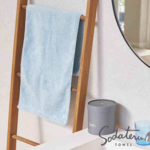 一條淺藍色、蓬鬆柔軟的毛巾，掛在木製毛巾架上。毛巾材質看起來輕盈，邊緣有流蘇。