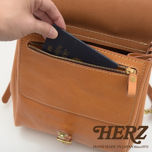 一只手將一本深藍色護照放入一個淺棕色皮革後背包的拉鍊口袋。後背包有明顯的縫線和金色拉鍊。