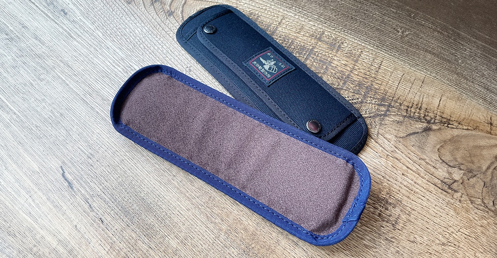 兩個黑犬印純棉帆布肩墊，一個為深藍色帆布，帶有品牌標籤和按扣；另一個為深紫色絨面，邊緣為深藍色滾邊。