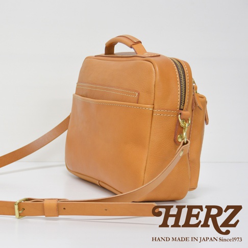 tan色職人手作皮革兩用多功能收納單肩包，包身方正，有拉鍊主隔層，正面有兩個開放式口袋，附可拆卸斜背帶及提把，側面有金屬扣環，整體線條簡潔，皮革材質自然。