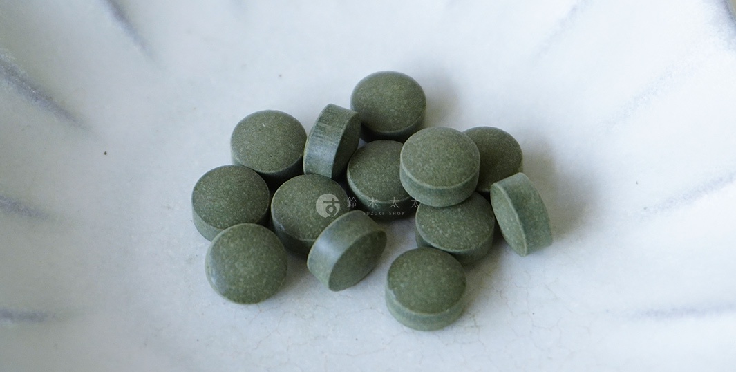一盤綠色圓形海苔錠，表面有些許紋理，其中有幾錠傾斜，盤底有細膩的紋路，盤中右側有「鈴木 SUZUKI SHOP」的白色浮水印。