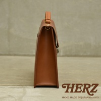 職人手作皮革Organ兩用商務公事包，呈現經典的棕褐色調，以高品質皮革製成，側邊視角展現其簡潔俐落的線條與精緻的縫線細節，配有金色金屬鎖扣和皮革提把，整體散發出低調的商務質感。