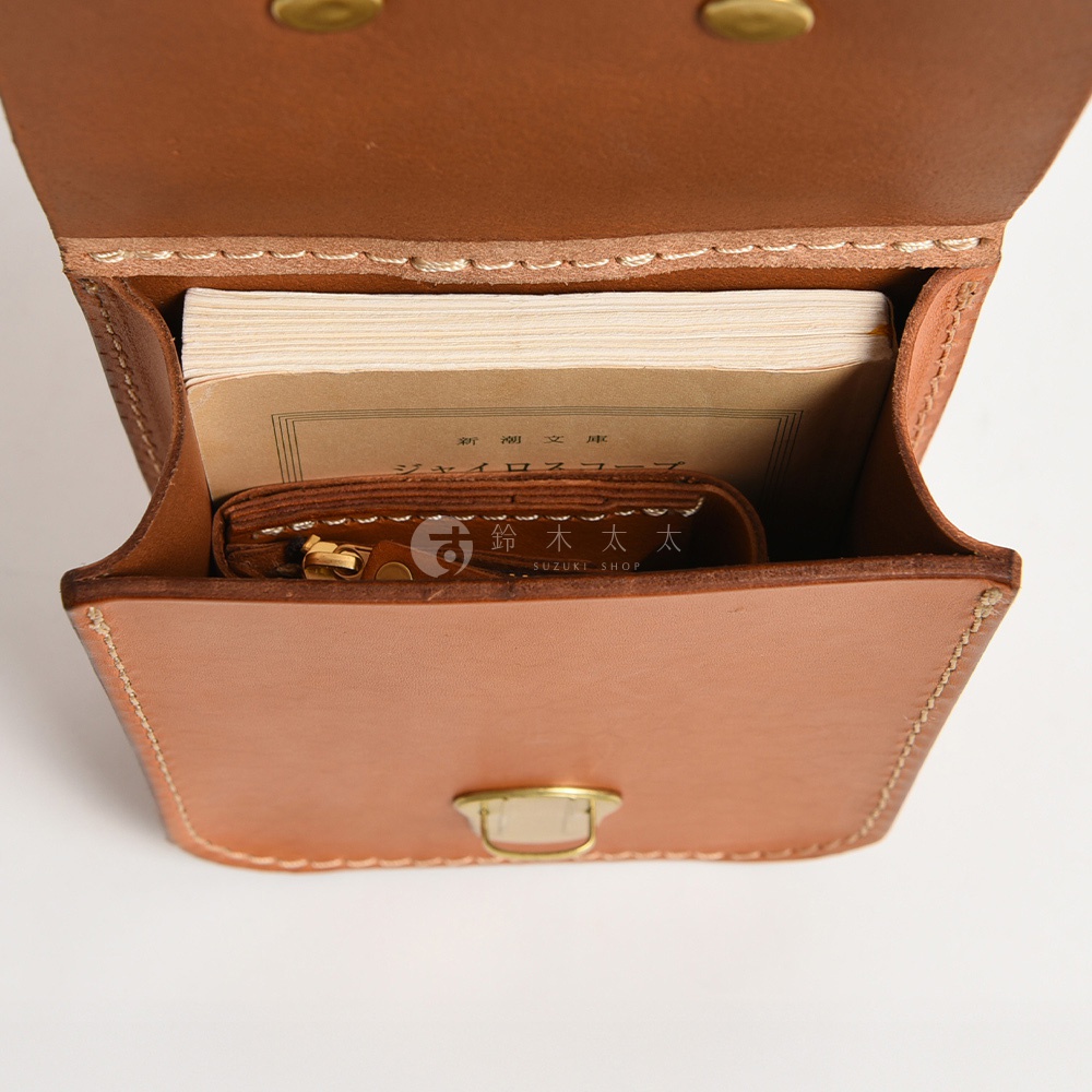 職人手作皮革經典腰袋，淺棕色調，全開式設計，內部可見一本淺色書本及一個附拉鍊的皮革零錢包，袋身縫線清晰，前方設有黃銅色金屬扣。