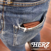 職人手作皮革旅行用雙層錢包，咖啡色皮革，部分置於牛仔褲後口袋中，展示錢包的材質與精緻工藝。