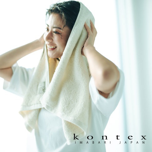 一位女性正露出開心的笑容，頭上披著潔白的 KONTEX KIYORA PREMIUM 雙效抗菌消臭大毛巾，柔軟的純白毛巾質感細膩，畫面充滿清新與舒適的氛圍，右下角標示著 KONTEX IMABARI JAPAN 的品牌名稱。