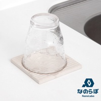 一個透明玻璃杯倒置在一個淺米色、帶有細微紋理的方形珪藻土置物墊上。置物墊放置在白色檯面上，背景是水槽的灰色邊緣。