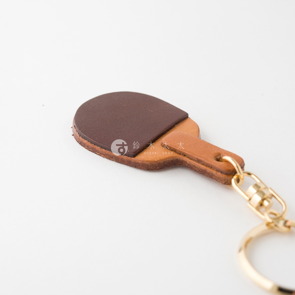 職人手作皮革桌球拍造型鑰匙圈，深棕色皮革拍面搭配淺棕色皮革拍柄，附有金色金屬掛環。