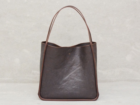 深棕色皮革方形托特包，配有細長的雙提把，包身縫線清晰，底部圓潤，中間有一個小金屬飾釘。