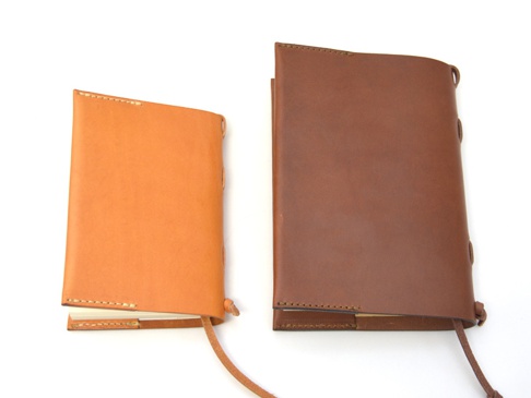 兩本職人手作皮革書套，一本為淺棕色，另一本為深棕色，皆附有皮革繩。