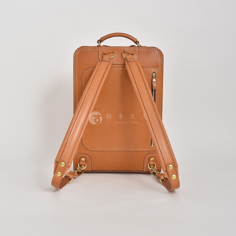 職人手作皮革商務電腦後背包 R-25，採用鞣製牛皮製成，呈現溫潤的焦糖棕色。雙肩帶可調節，配有黃銅色五金扣環及拉鍊，設計簡約實用。