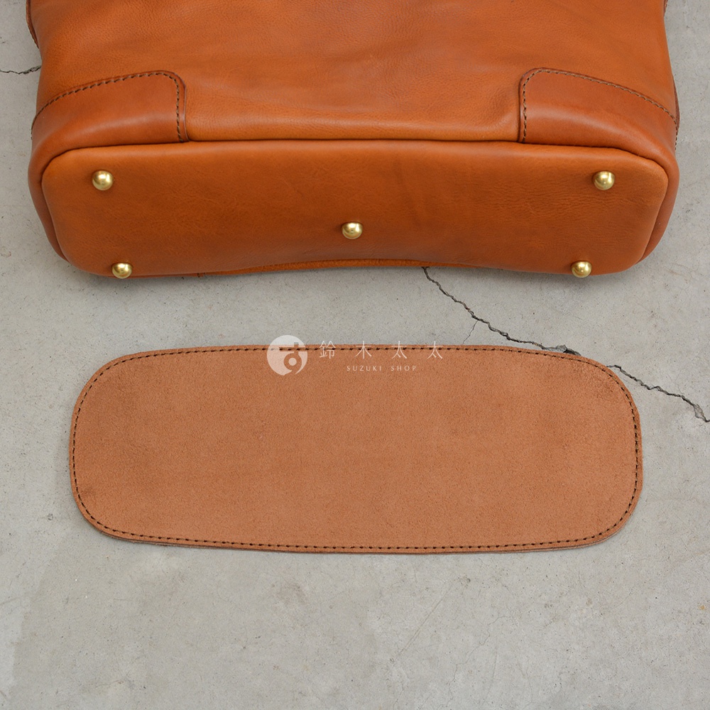 棕色皮革托特包底部與一個相同材質的扁平皮革配件，底部裝有四個黃銅色的金屬腳釘