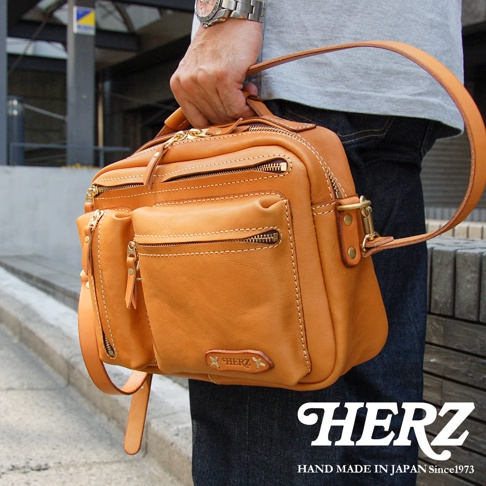 職人手作皮革兩用多功能收納單肩包，天然皮革材質，呈現溫潤的焦糖色。包身結構立體，設有多個拉鍊口袋，包括前側兩個立體小口袋，設計精緻實用，適合日常攜帶。
