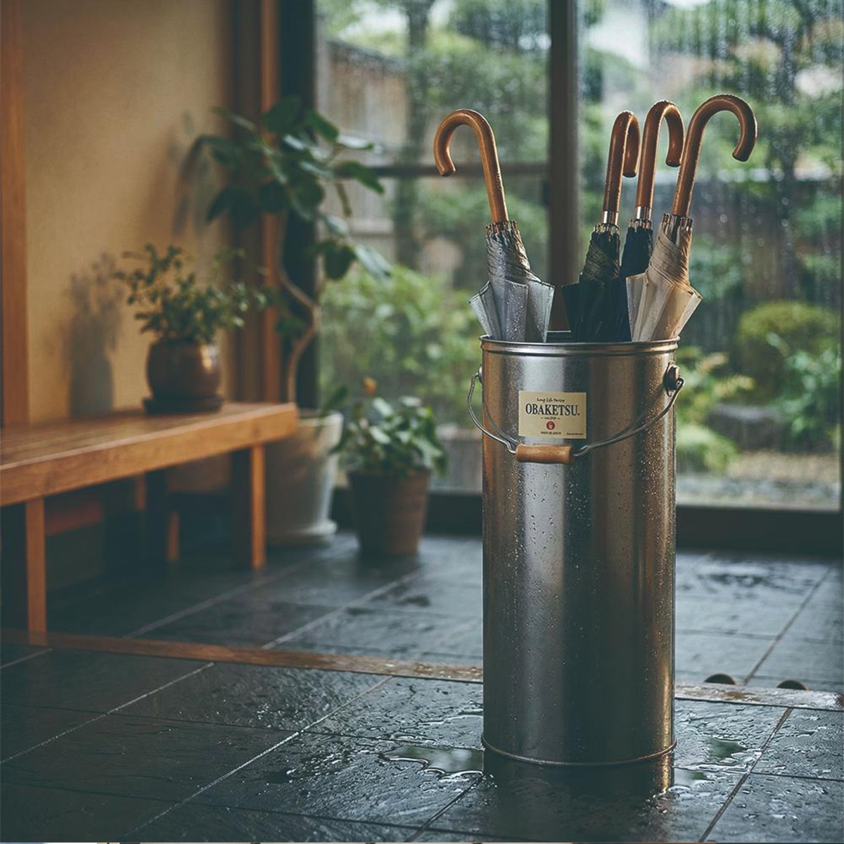 OBAKETSU 手工製傘桶，置於雨天濕滑的地面上，桶內有幾把木柄雨傘。