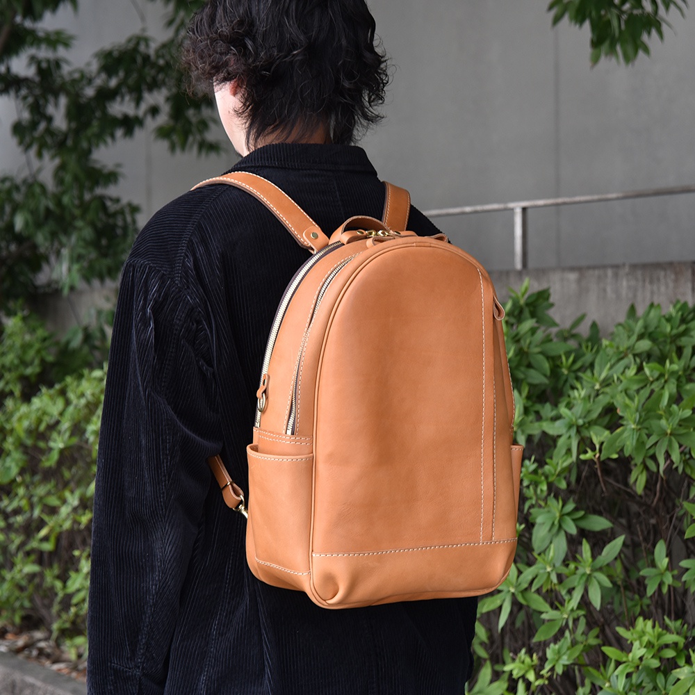 棕褐色皮革多功能後背包，設有拉鍊主隔層、正面拉鍊口袋和側袋，以簡潔的白色縫線裝飾。