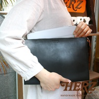 一位女士手持一個黑色皮革手拿包，包身簡約，頂部有拉鍊和品牌標誌。包內裝有一個淺灰色平板電腦。