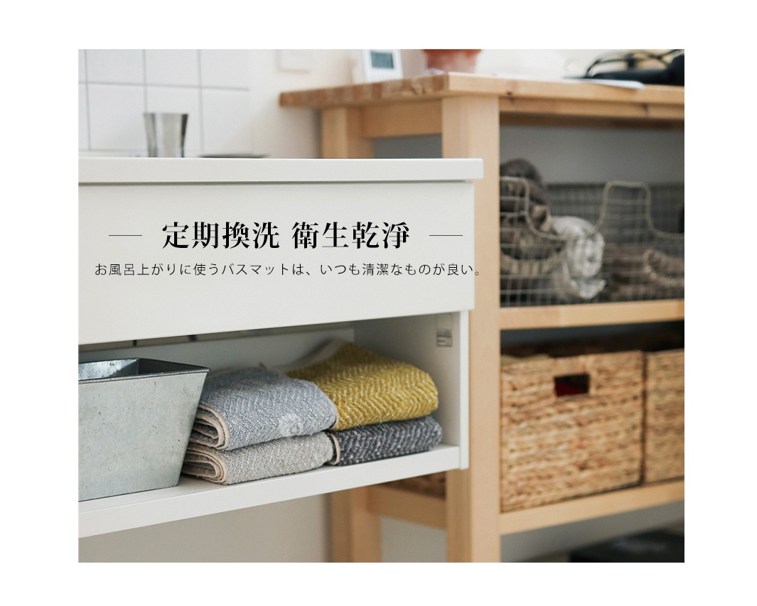 白色收納櫃下方層架上，擺放著一個銀灰色金屬方盆，以及疊起的毛巾。毛巾有黃色、灰色及深灰色，材質看來為織物。