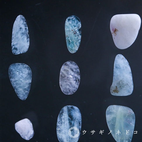 九塊不規則形狀的細石標本，顏色從淺藍、藍綠到乳白色不等，部分標本帶有雲霧狀紋理或細微雜質，材質應為礦石。