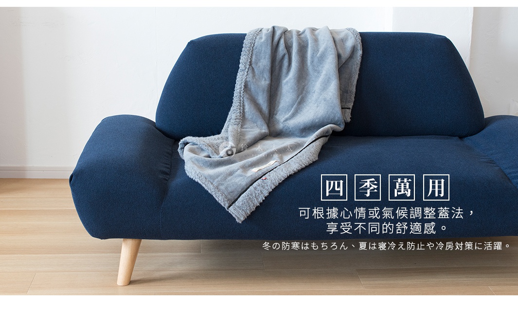 藍色沙發上搭著一條淺灰色、羊毛感材質的膝蓋毯，毯子邊緣有絨毛滾邊，毯身上印有細小的花紋和品牌標誌。