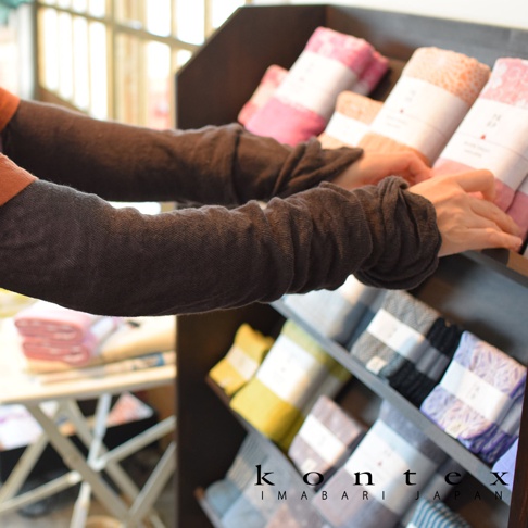 兩隻深棕色棉麻混紡彈性袖套，質地輕薄，袖口有皺褶設計，展示於木製架上。