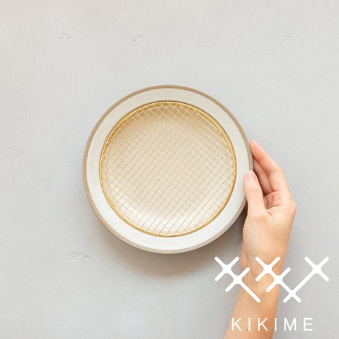手持一個米白色美濃燒餐盤，盤內有一個金色細網，盤緣為淺棕色。