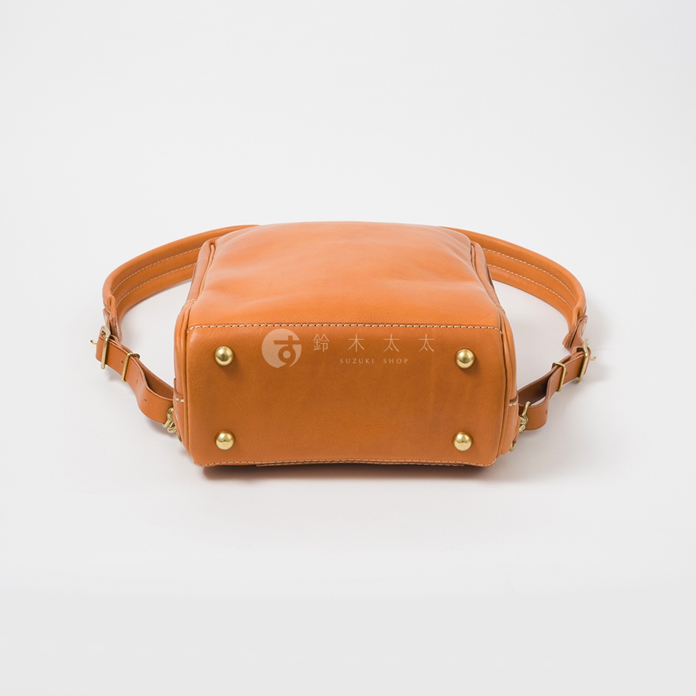 手作皮革軟皮商務後背包，呈現溫暖的橘棕色調，搭配金屬腳釘與可調節的皮革背帶，展現精緻工藝。