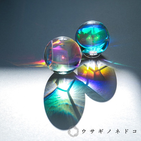 合光稜鏡球，兩個透明的水晶球，表面反射著彩虹般的光芒，散落在灰色背景上，投射出色彩斑斕的陰影。