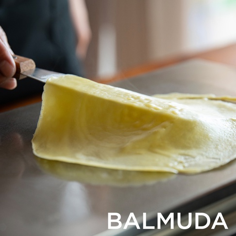 The Plate Pro 極致電烤盤 (黑色) 表面正在烹調一層金黃色的薄餅，一隻手持金屬刮刀，正在將薄餅的一角從烤盤上分離。