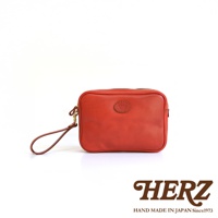 橘紅色皮革手提包，配有可拆卸的皮質腕帶和金色扣環，正面中央有橢圓形品牌壓印。